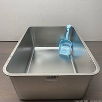 Full view of empty metal cat litter box with blue scoop resting inside.