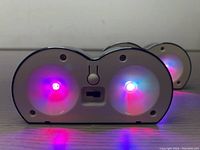 Close-up photo of two small solar lights emitting purple and red LED light with visible switch and solar panel area on back.