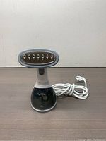 Photo showing front view of fabric steamer with steam nozzle, base, and power cord laid beside.