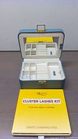 Open light blue jewelry box with visible compartments and a mirror on inside of lid, positioned behind a Cluster Lashes Kit box with yellow and cream colored packaging.