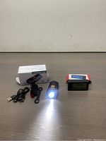 Wastou LED bicycle lamp lit, with USB charger cable, mount, and digital clock/thermometer/LED light unit in box on table.