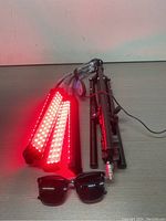 LED grow light panels emitting red light, foldable metal stand, and protective sunglasses laid on floor.