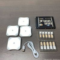 Four square Bestendony LED lights, USB cable, and pack of 12 LED G9 bulbs on gray surface, arranged and visible clearly.