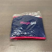 Front view of Magic Gel neck ice pack in original plastic packaging, showing navy blue fabric and pink trim with logo