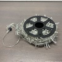 Top view of the coiled outdoor Christmas string lights on the black plastic reel showing clear bulbs and wired plug.