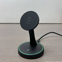 Front view of black magnetic wireless charger with glowing green ring and phone icon on top, showing charging stand and power cable.
