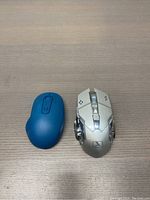 Top view of the blue wireless computer mouse and silver gaming mouse placed side by side on a wooden surface