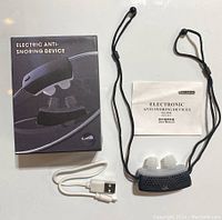 Electric anti-snoring device with USB cable and user manual displayed on a white surface.