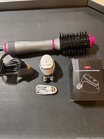 Photo showing Remington ceramic hair straightening brush, 5-in-1 microcurrent beauty massager, its charging cable, plug adapter, and product box on a surface.