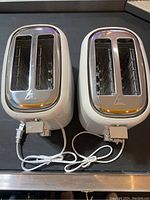 Two white Hamilton Beach 2-slice toasters side by side. Both have chrome accents and extra-wide slots. White power cords are visible.