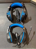 Two wired gaming headsets with blue and black cushioning, microphones attached, resting on a black surface.