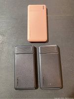 Three power banks arranged on black surface, two black and one pink, showing size and color variation in set