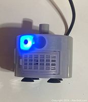 Front view of the submersible water pump showing the inlet grid, suction cups on the base, and blue LED indicator light powered on.