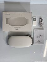 Box of AMAZMASS GLAD-1 waist and abdomen massager, remote control, USB charging cable, instruction manual, and the massager device outside the box on a white surface.
