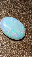 Oval cabochon Ethiopian opal with vivid rainbow colors on textured brown background.