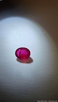 Oval cut blood red pink ruby gemstone under spotlight showing vivid color and clarity