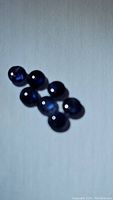Seven deep blue round cabochon blue sapphires placed on a white background showing polished surface and inclusions.