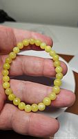 Front photo of a natural lemon jade bracelet held between fingers showing smooth, round yellow beads about 6mm each.