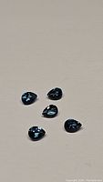 Five pear cut London Blue Topaz gemstones arranged on a plain surface showing facets and color.