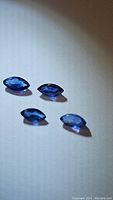 Photo of four marquis cut blue sapphires arranged on light surface, showing facets and shape.