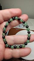 Bracelet held in hand showing green and black polished round beads on elastic band