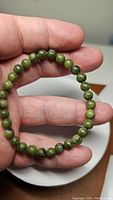 Hand holding a natural jade bracelet made of 6mm round green beads on a stretchy band.