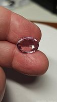 Close-up image of natural pink amethyst gemstone held between fingers, showing the oval cut, facets, and pink color.