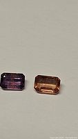 Two emerald cut sapphires side by side, one purple-pink and one orange, showing cut style and color
