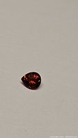 Close-up photo of a pear-shaped faceted spessartite garnet gemstone on a white background showing its deep orange-red fire color and internal reflections.
