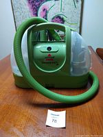Front view of green Bissell Little Green portable cleaner with hose coiled in front and clear water tanks on sides.