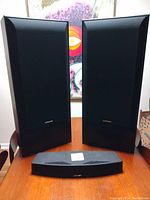 Two Pioneer tall tower speakers and one Bose center channel speaker positioned on a wooden table, front view with grills on the tower speakers.