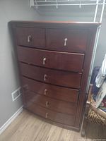 Photo of a tall, dark wood dresser with six drawers, two smaller top drawers and four larger bottom drawers, each with a metallic drop pull handle.