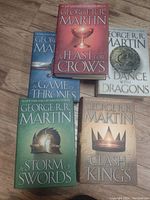 Five paperback George R.R. Martin novels from the 'A Song of Ice and Fire' series laid out on a wooden floor.