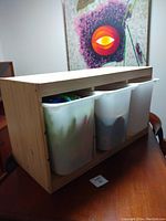 Side view of wooden storage frame with three white plastic bins inside, showing front bins filled with items.