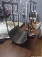 Iron log stand or holder viewed from an angle on a table, showing its curved cradle and four vertical support bars with rivet details.