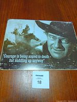 Metal sign featuring John Wayne's face and a cowboy on horseback with a memorable quote.