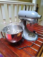 Photo of KitchenAid Artisan stand mixer in silver color showing the base, mixing bowl, wire whisk and flat beater attachments.