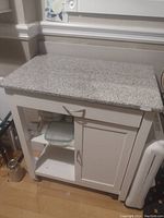 Full view of white kitchen storage cart with stone countertop, drawer, cabinet door, and lower shelves.