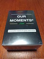 Box of Our Moments Kids conversation starter cards sitting on a wooden surface, front facing, showing brand and purpose of cards.