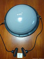 Top view of gray half ball balance trainer with black base and attached resistance bands with foam handles spread out on wooden surface.