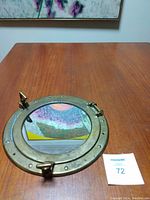 Closed view of the brass porthole mirror showing reflective glass and brass frame with rivet details and latches.