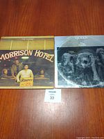 Photo showing vinyl record covers of Queen's 'The Game' and The Doors' 'Morrison Hotel' on a wooden surface.