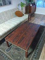 Full view of rosewood veneer coffee table placed on patterned rug in living room setting with sofa in background.