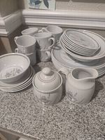 Full view of the dinnerware showing stacked plates, cups, bowls, sugar bowl and creamer with blue iris design.