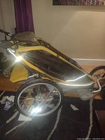 Side angle photo of running stroller showing yellow and black exterior, large wheels, and metal frame.