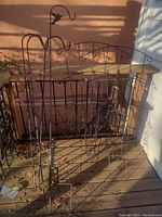 Four tall slender shepherd hook stakes and two metal trellises side by side outdoors on wood deck.