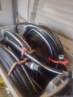 Three coiled black garden hoses with silver click connect fittings, secured with red bands, placed in a container.