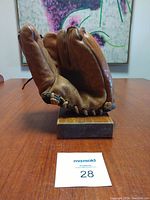 Vintage brown leather baseball glove mounted on a wooden display stand shown on table with background art visible.