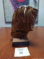 Side view of vintage brown leather baseball glove mounted on a wooden stand, showing front side and glove fingers.