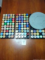 Overview of three trays filled with over 110 vintage film slide containers and a large gray film reel canister on wooden table.
